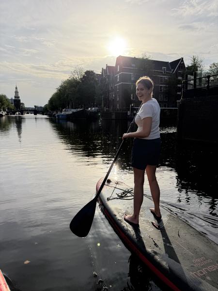 A person is joyfully stand-up paddleboarding on a sunny canal in Jodenbreestraat, Uilenburg, Amsterdam